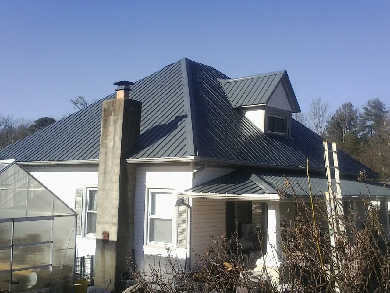 Dark blue standing seam metal roof on a white farmhouse with dormer — Slate & Tile Roof Repair by Roofing Brothers in Porum