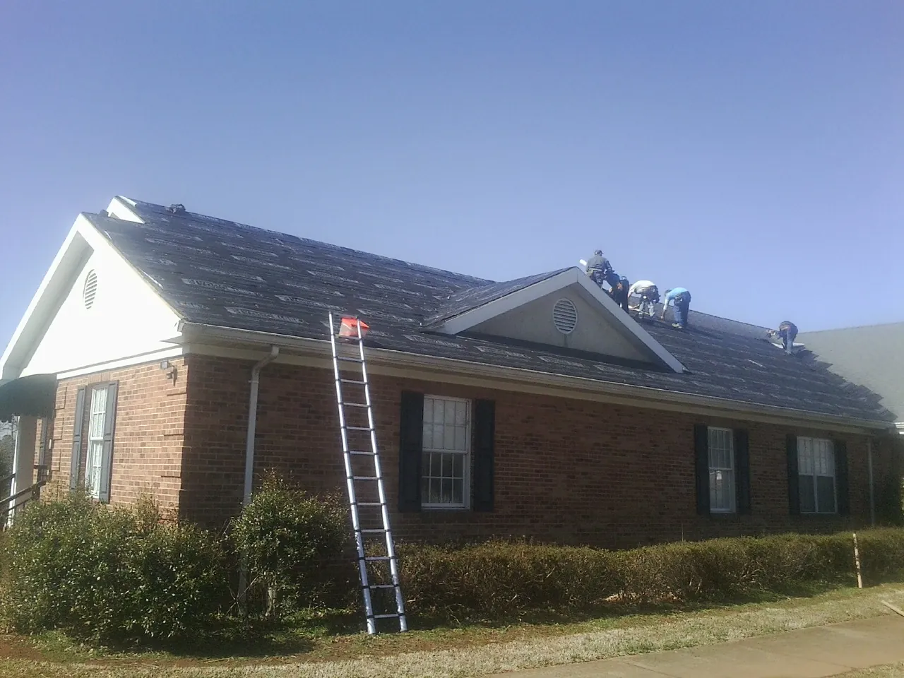 Crew tearing shingles off a brick ranch roof with a ladder set — Emergency Roof Repair work by our crew in Porum