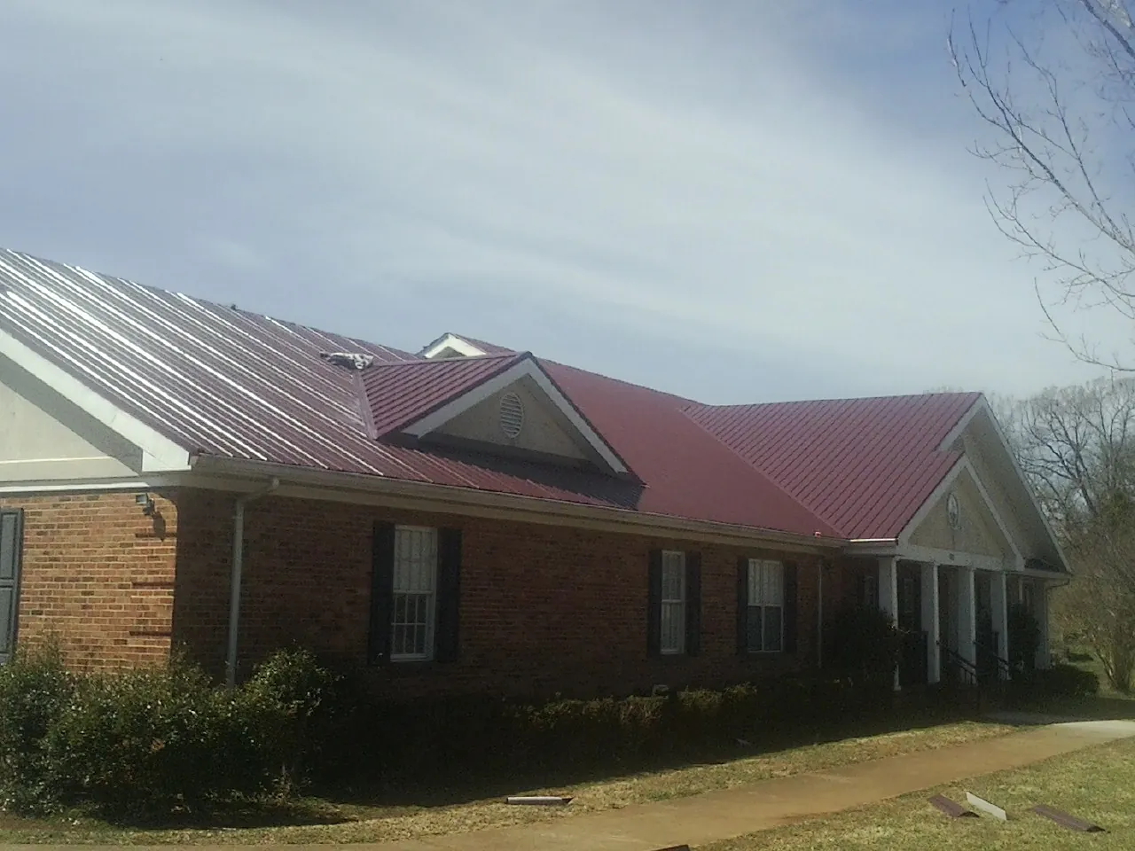 Red metal roof with gabled entries on a long brick building, from a Hail Damage Roof Repair job in Porum