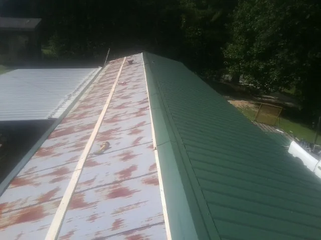 Old rusted panels beside newly installed green metal roofing — Wind Damage Roof Repair by Roofing Brothers in Porum