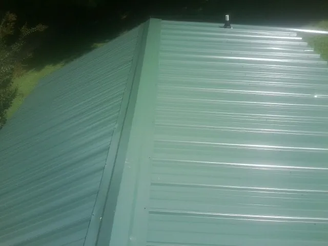 New green metal panels meeting at the ridge of a roof — Flat Roof Repair work by our crew in Porum