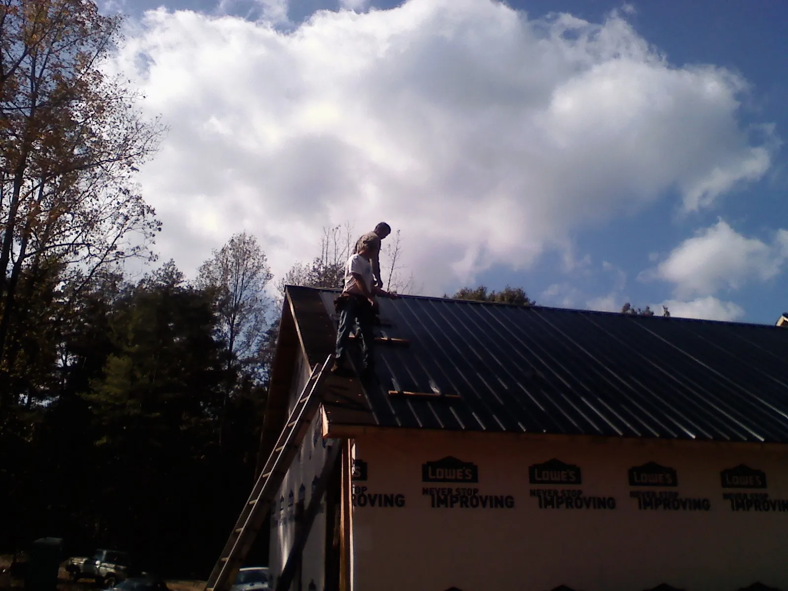 Roofer fastening dark metal panels high against a cloudy sky, from a Roof Inspection job in Porum