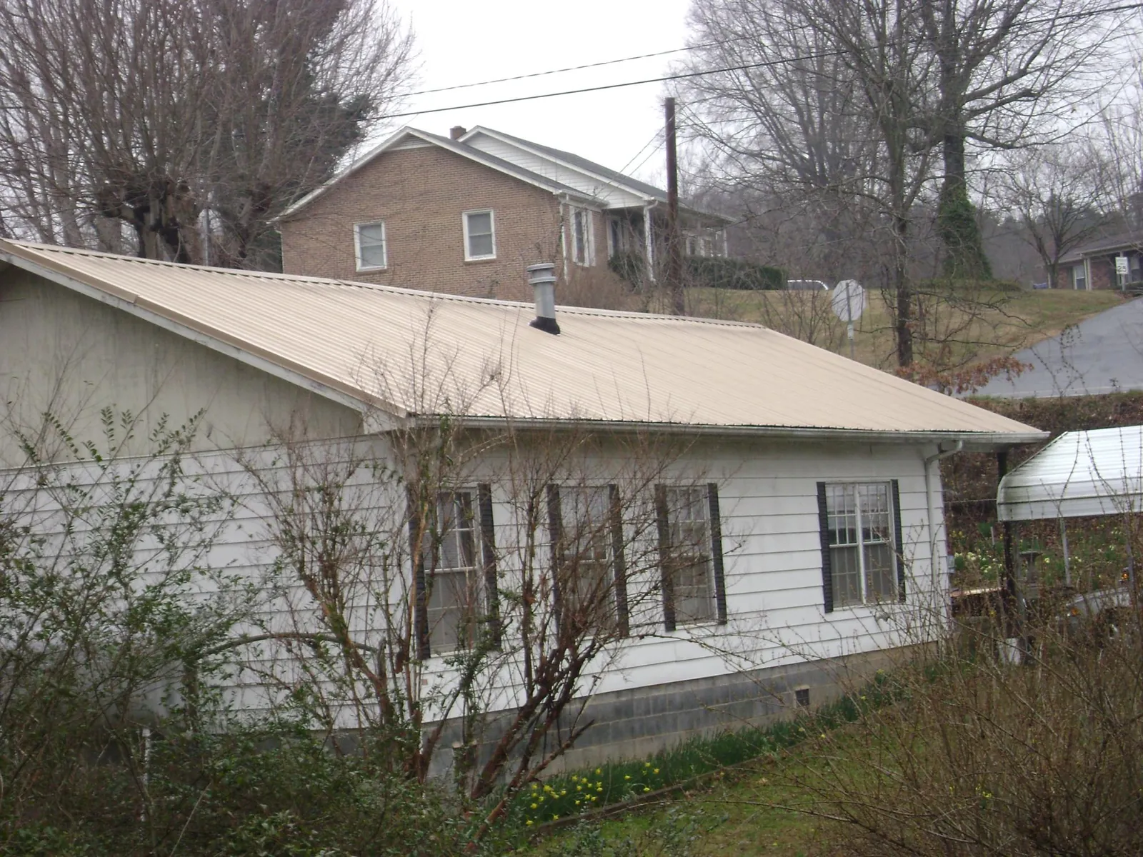 Tan metal roof on a white sided house set into a hillside — Commercial Roofing by Roofing Brothers in Porum