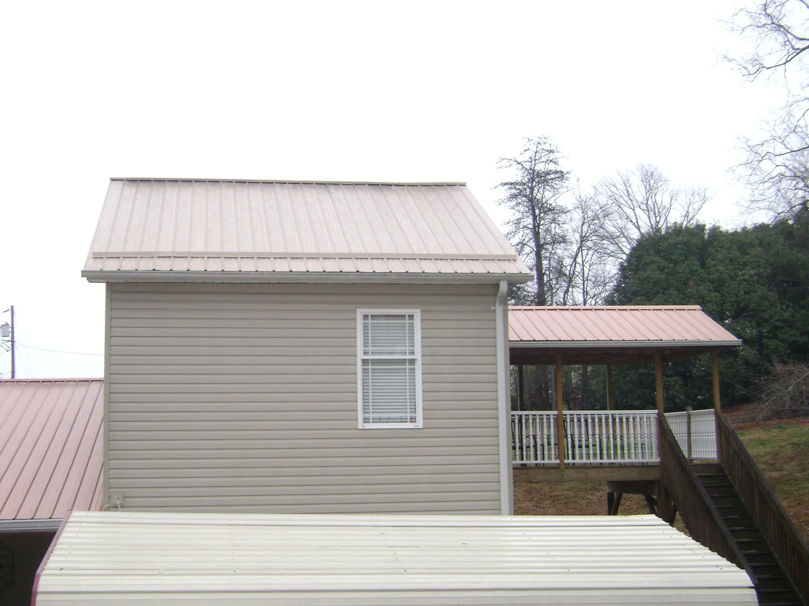 Tan metal roofs on a two story addition and attached porch, from a Roof Replacement job in Porum